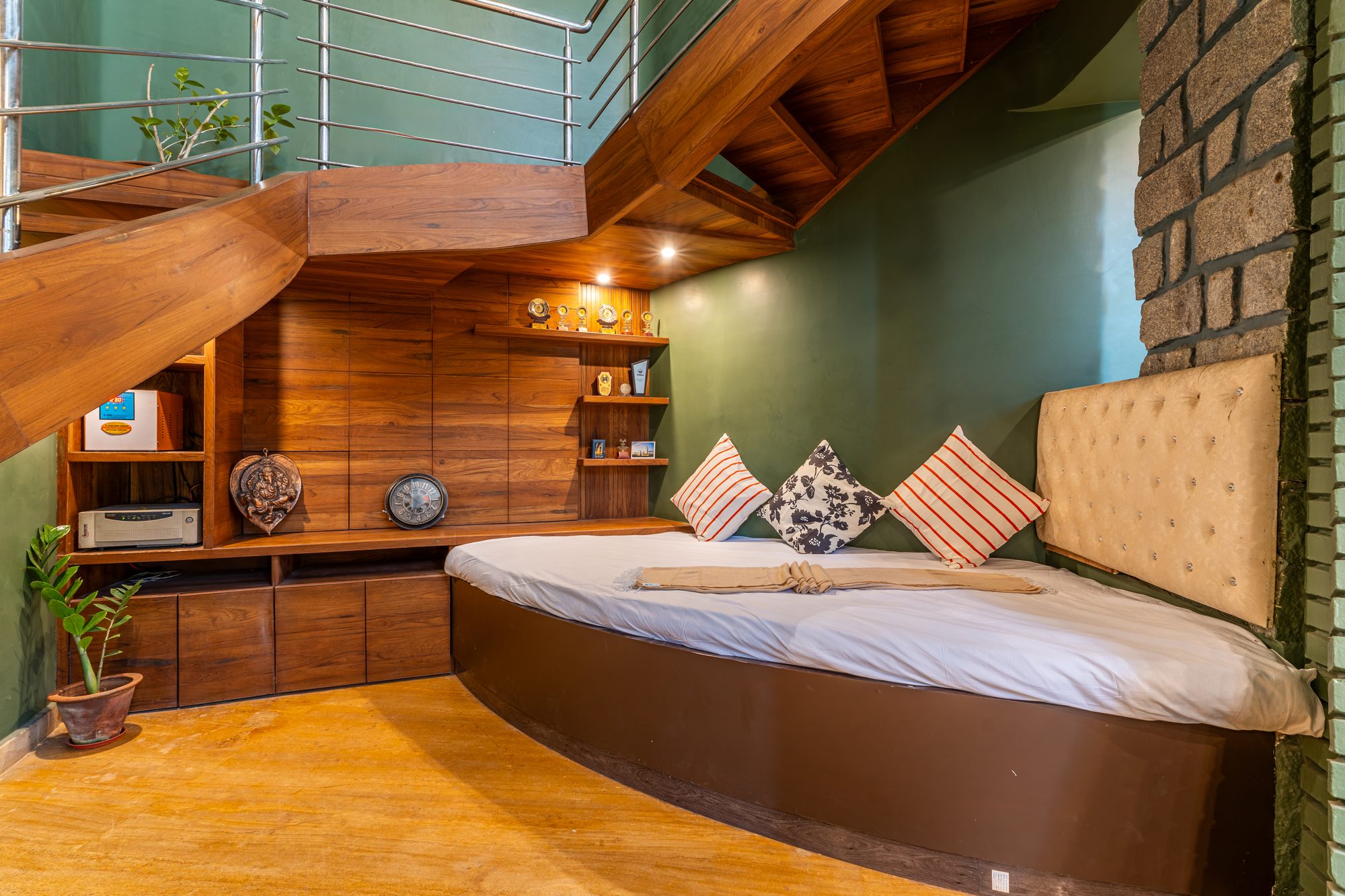 Day bed tucked under the spiral staircase, with a wood-paneled shelf of trophies and a stone accent wall