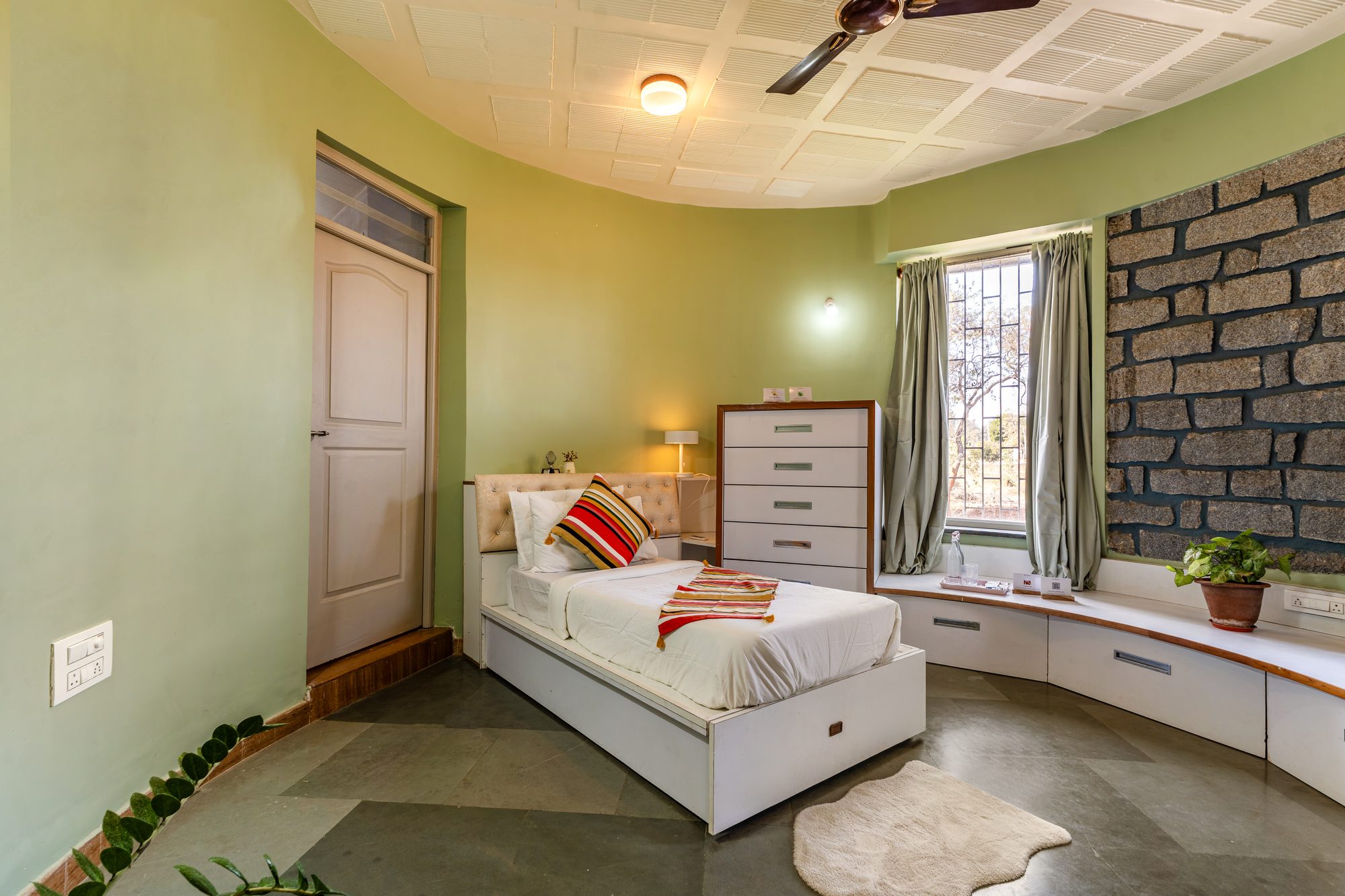 Day bed with a single mattress, olive-green curved walls, stone accent wall and a built-in window bench
