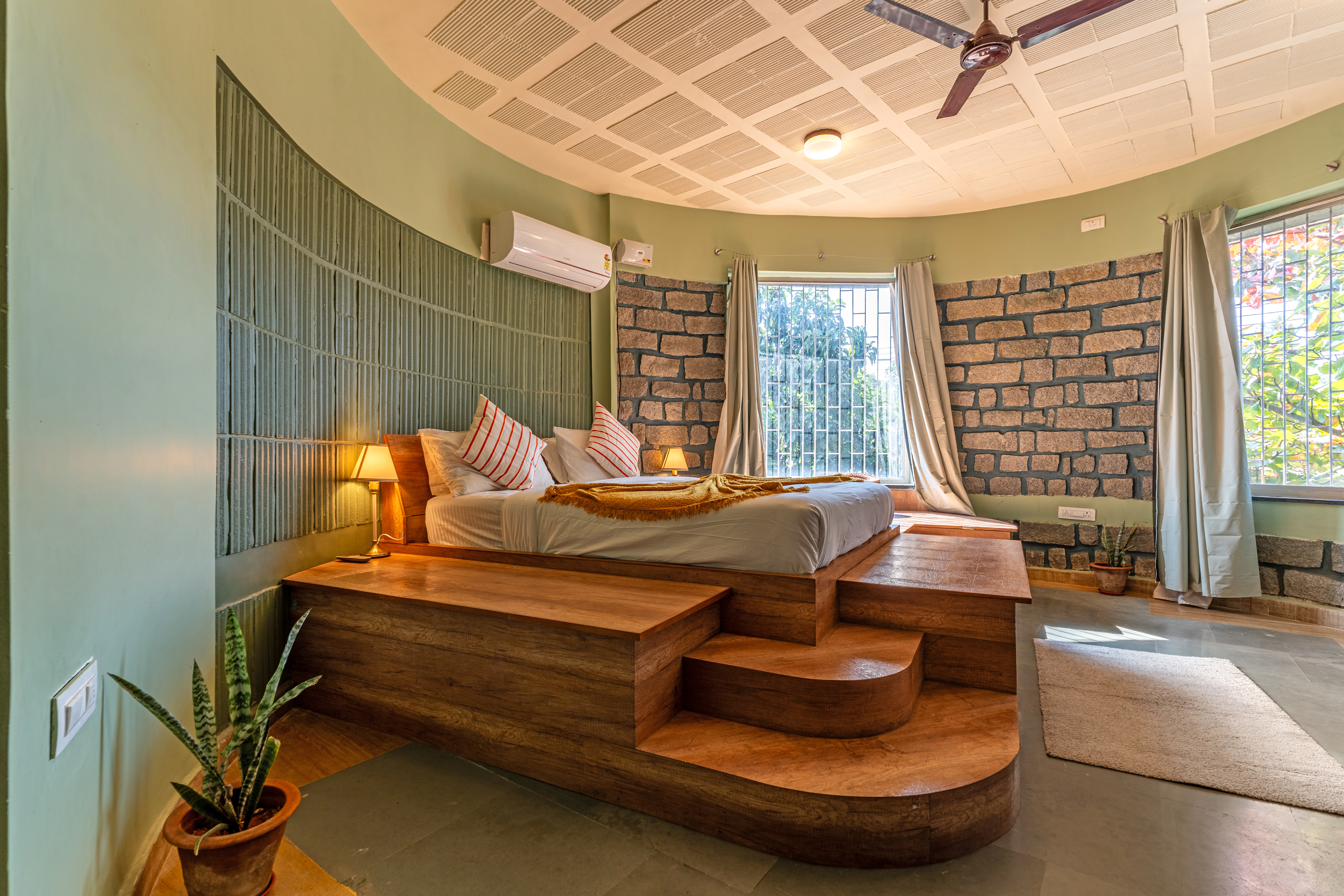Bedroom with a raised circular wooden platform bed, square-grid coffered ceiling, ceiling fan and stone accent wall