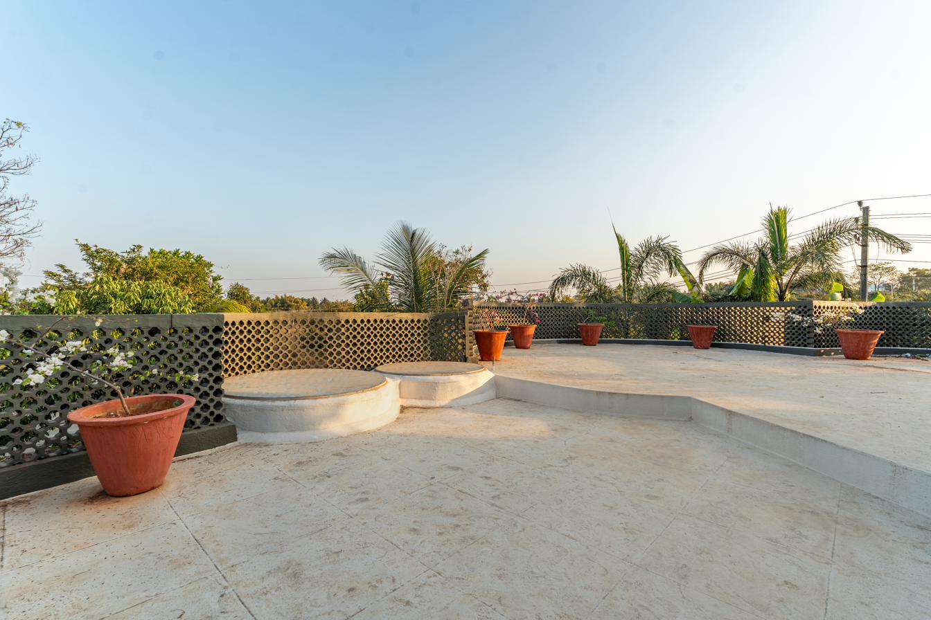 Open rooftop terrace with lattice parapet wall, circular concrete benches and terracotta pots